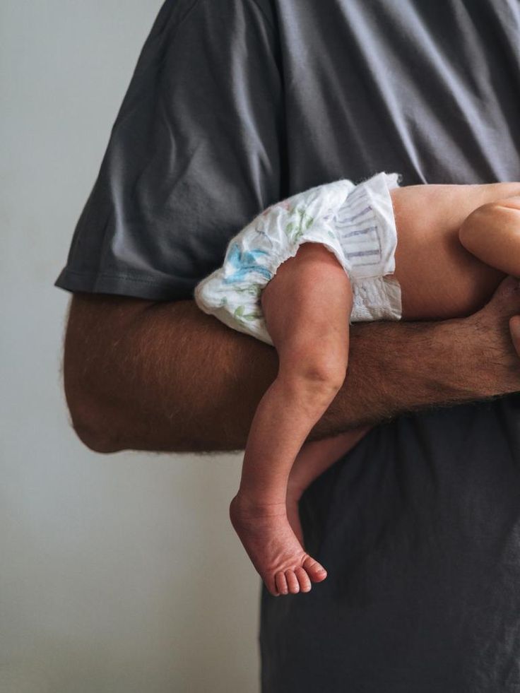 Pai segurando bebê recém-nascido no antebraço em posição avião, técnica indicada por pediatras para aliviar cólica em bebês, ilustração de artigo sobre cólica em bebê por pediatra particular em Belo Horizonte